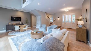 A spacious living room with a high ceiling, a dining area with a round table and chairs, and a staircase leading to an upper level. - Sycamore Ranch (Templeton)