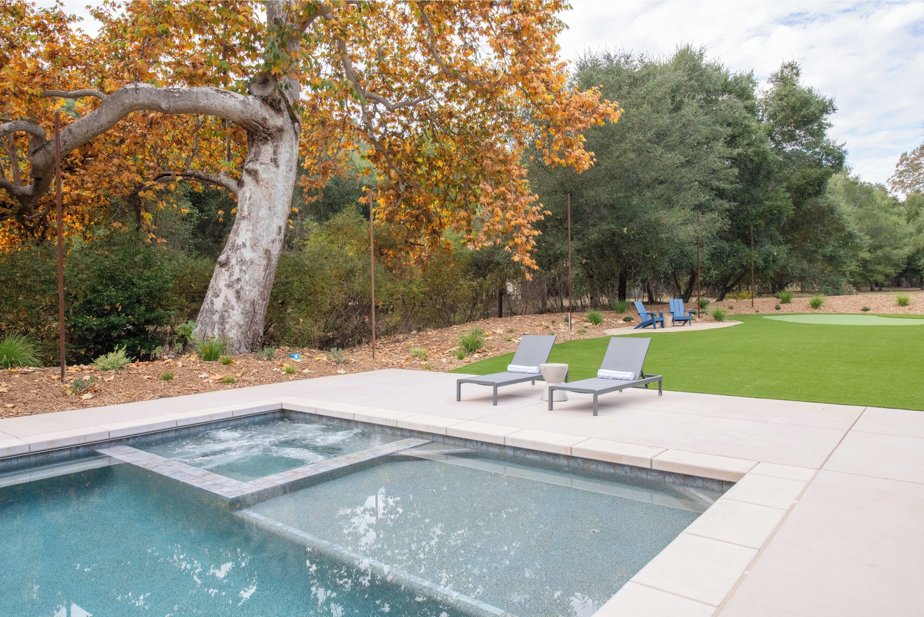 A swimming pool with two lounge chairs and a tree with autumn leaves.