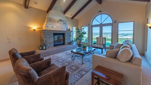 A living room with a stone fireplace, leather chairs, a sofa, a coffee table, and large windows offering a view. - Paso Palacio (Paso Robles)