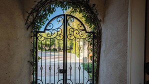 A wrought iron gate with intricate designs, leading to a paved pathway. - Paso Palacio (Paso Robles)