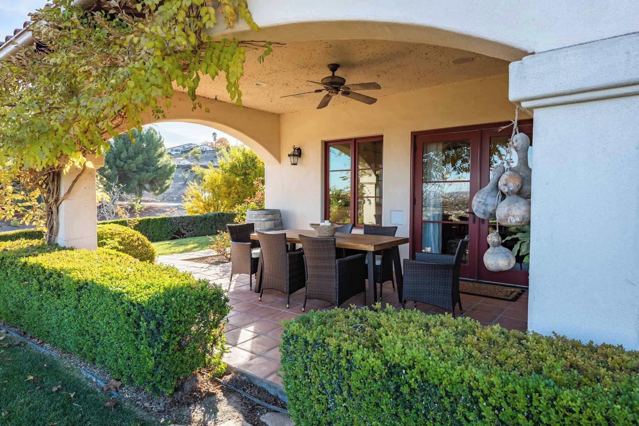 An outdoor patio with a table and chairs, a ceiling fan, and a view of the surrounding landscape.