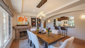 A dining area with a wooden table, white chairs, a fireplace, and a kitchen in the background. - Paso Paradiso (Paso Robles)