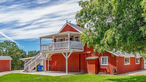 A two-story red building with a balcony, a covered porch, and a small attached shed. - Red Barn Loft (Templeton)