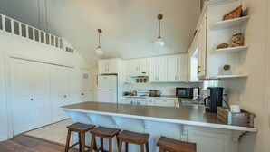 A kitchen with white cabinets, a large island with stools, a microwave, and a refrigerator. - Red Barn Loft (Templeton)