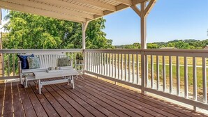 A covered outdoor deck with a white bench and railing, overlooking a grassy area and trees. - Red Barn Loft (Templeton)