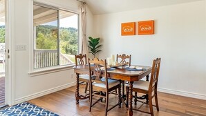 A dining area with a wooden table and chairs, a view through a sliding glass door, and two framed pictures on the wall. - Red Barn Loft (Templeton)