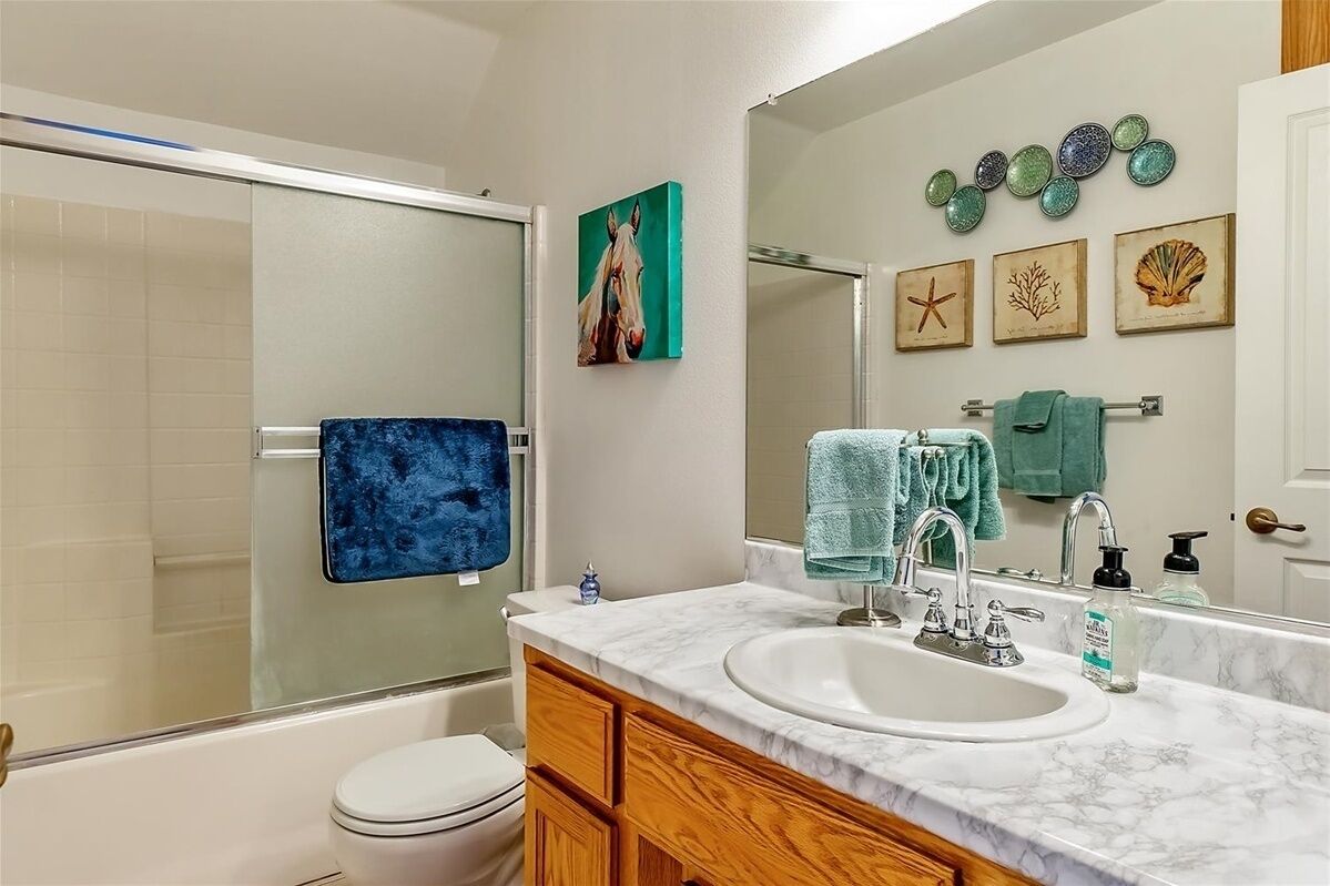 A bathroom with a bathtub, toilet, vanity with a sink, and a mirror. There are decorative items on the wall and a towel rack with towels.