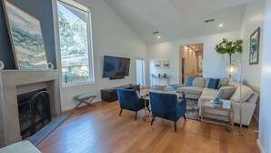 Un salon moderne avec une cheminée, un téléviseur à écran plat, un canapé, deux fauteuils bleus et une table basse.