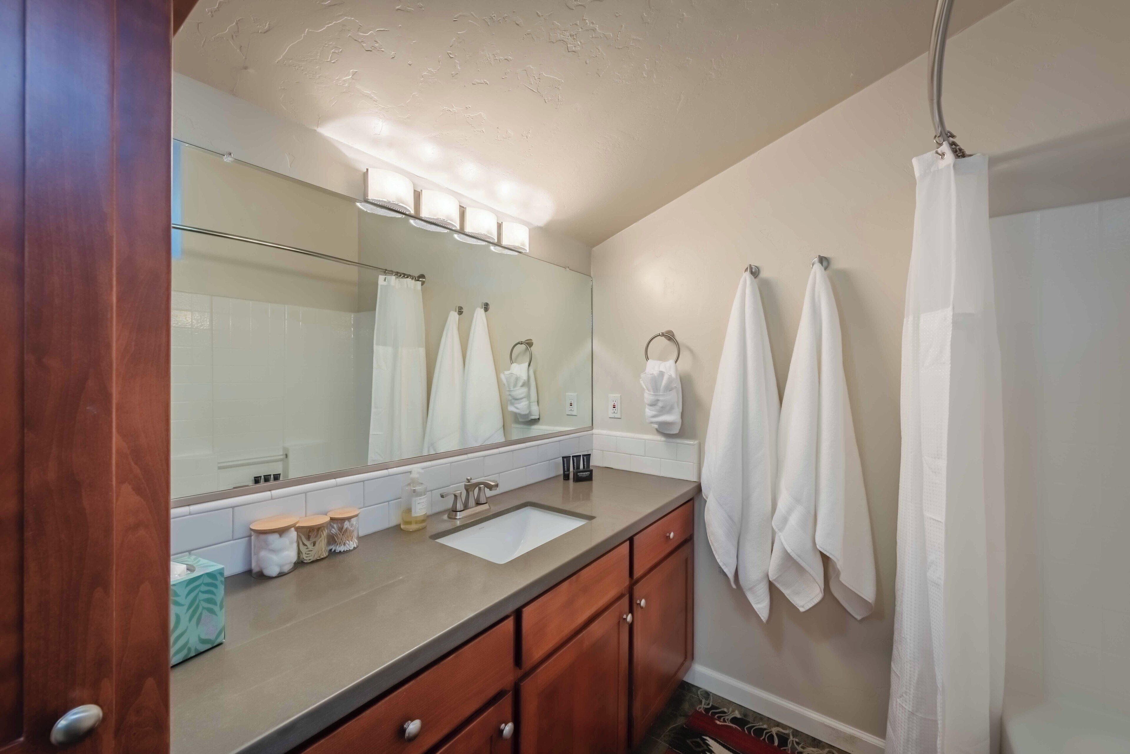 A bathroom with a wooden vanity, a sink, a mirror, and a shower curtain.