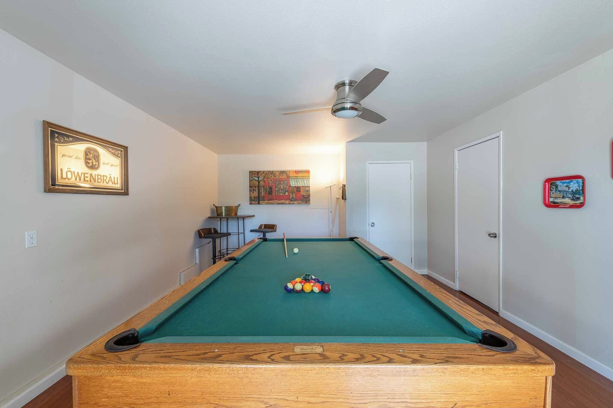 A pool table with balls, a ceiling fan, a framed sign, and a door.