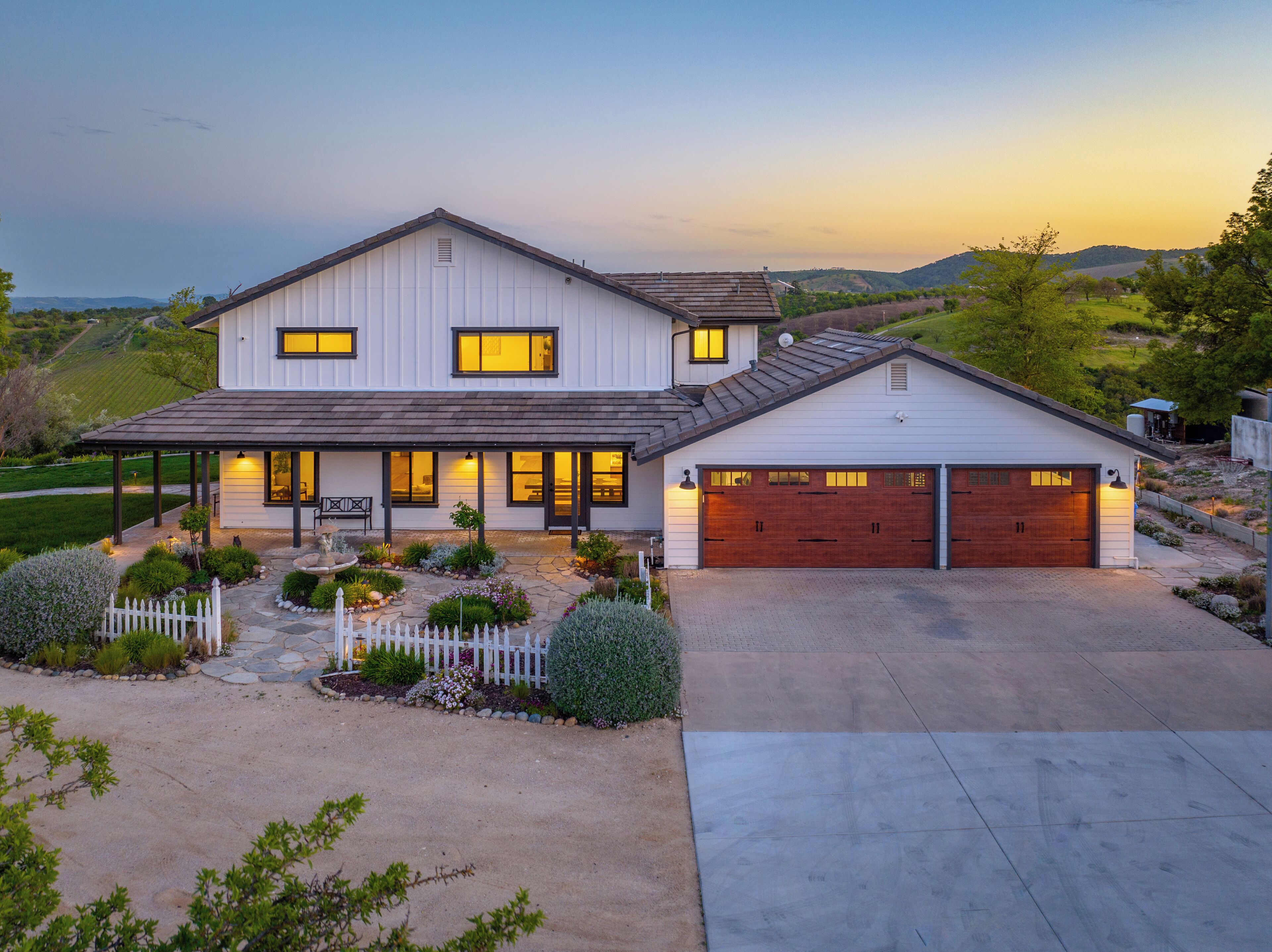 A two-story house with a garage, a covered porch, and a landscaped front yard with a white picket fence.