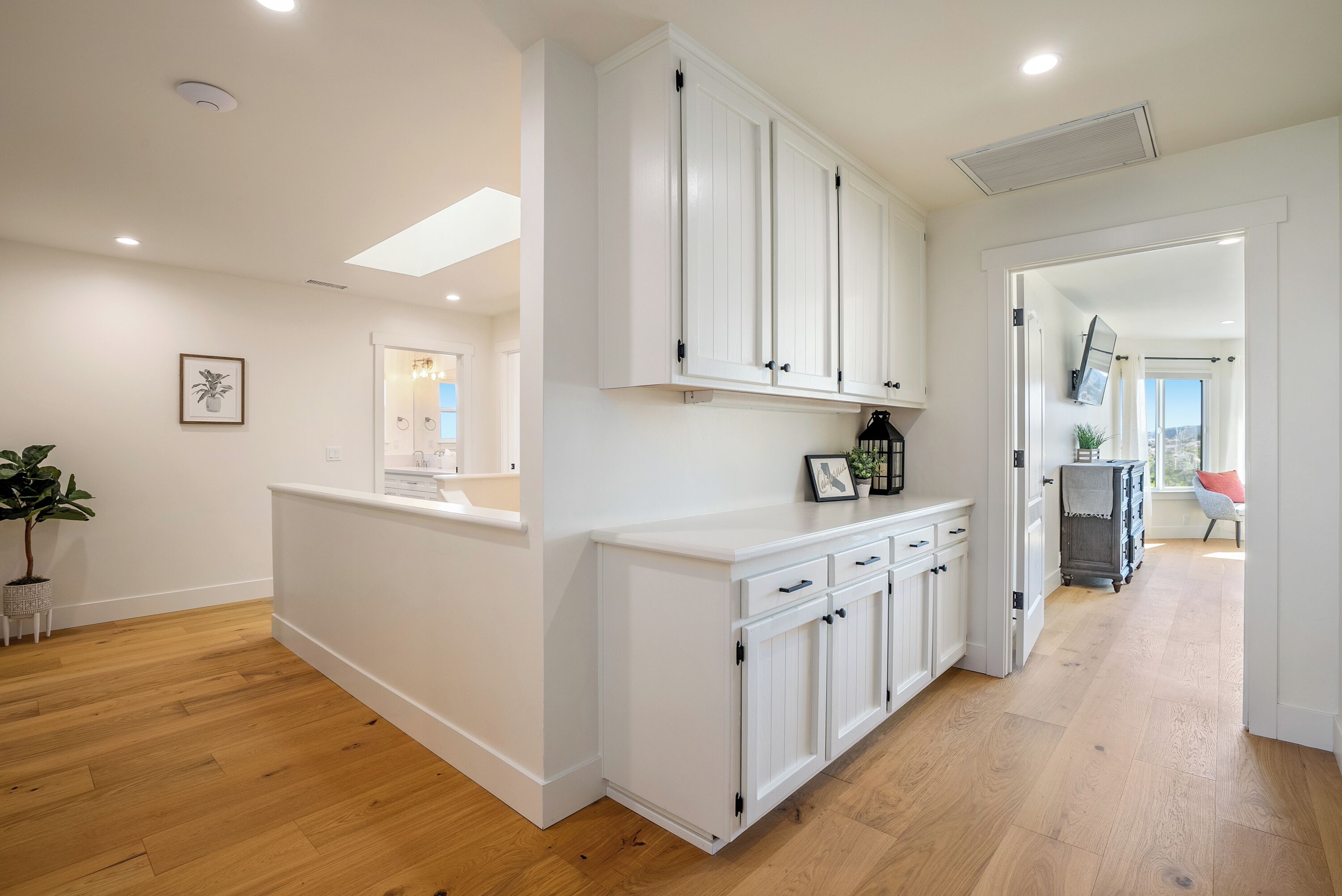 A modern kitchen with white cabinetry, wooden flooring, and a view to the living area.