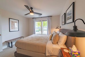 A bedroom with a bed, ceiling fan, bedside table, lamp, and artwork on the walls.