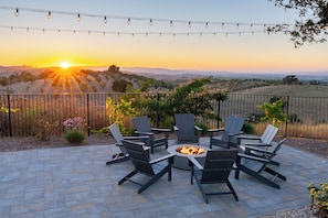 A patio with a fire pit and chairs, overlooking a landscape with a sunset. - Hilltop Oasis (Templeton)