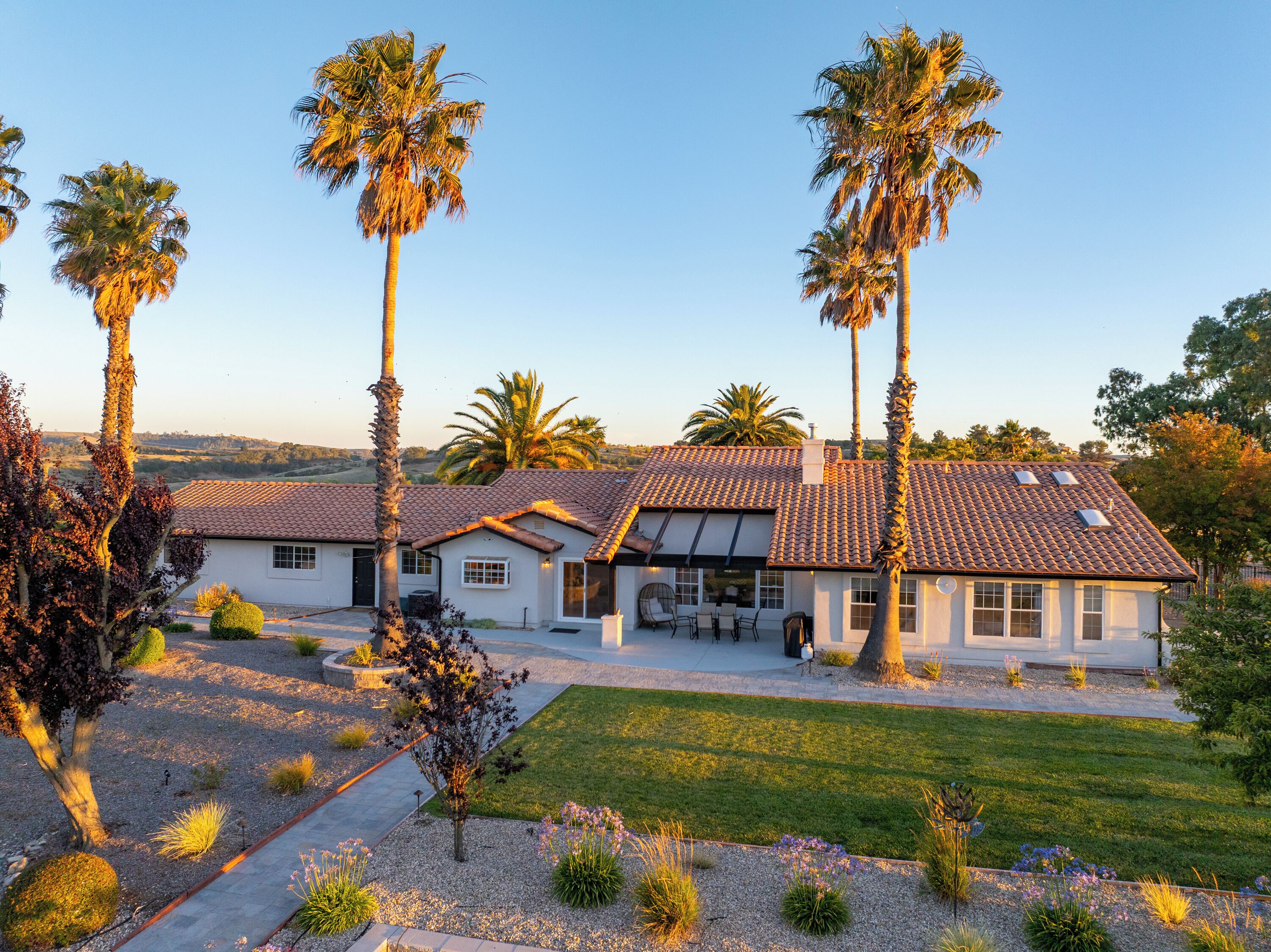 A two-story house with a tiled roof, surrounded by a well-maintained lawn and palm trees.
