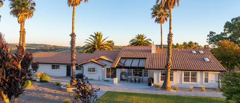 A two-story house with a tiled roof, surrounded by a well-maintained lawn and palm trees.