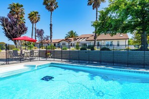 A swimming pool with a red umbrella, surrounded by palm trees and a house with a tiled roof. - Hilltop Oasis (Templeton)