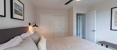 A bedroom with a bed, a ceiling fan, a bedside lamp, and framed pictures on the wall.