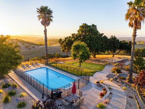 A swimming pool with a surrounding deck, seating area, and a view of a hilly landscape.