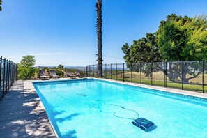 A rectangular swimming pool with a clear blue water, surrounded by a black fence, and a few lounge chairs.