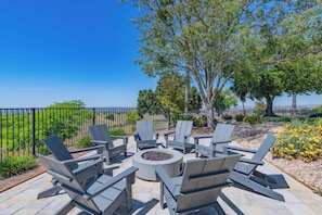 An outdoor seating area with Adirondack chairs and a circular fire pit, surrounded by a stone patio and a view of the landscape. - Hilltop Oasis (Templeton)