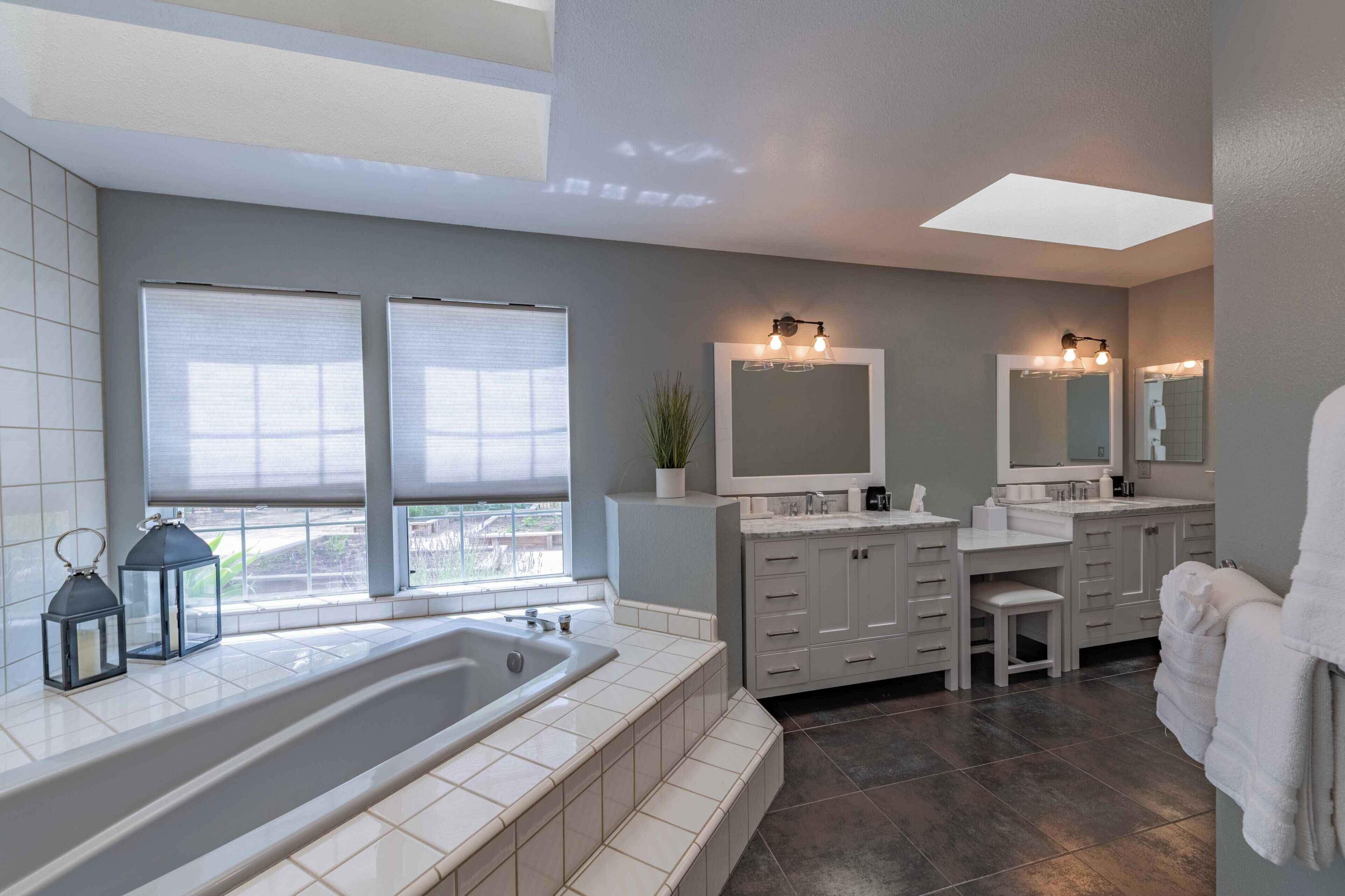 A modern bathroom with a large bathtub, two sinks, and a vanity with a mirror.