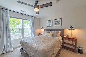 Una camera da letto con un letto, una ventola a soffitto, lampade sui comodini e una finestra con tende.
