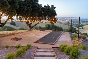 An outdoor seating area with a view of the countryside, string lights, and a wooden bench. - Hilltop Oasis (Templeton)
