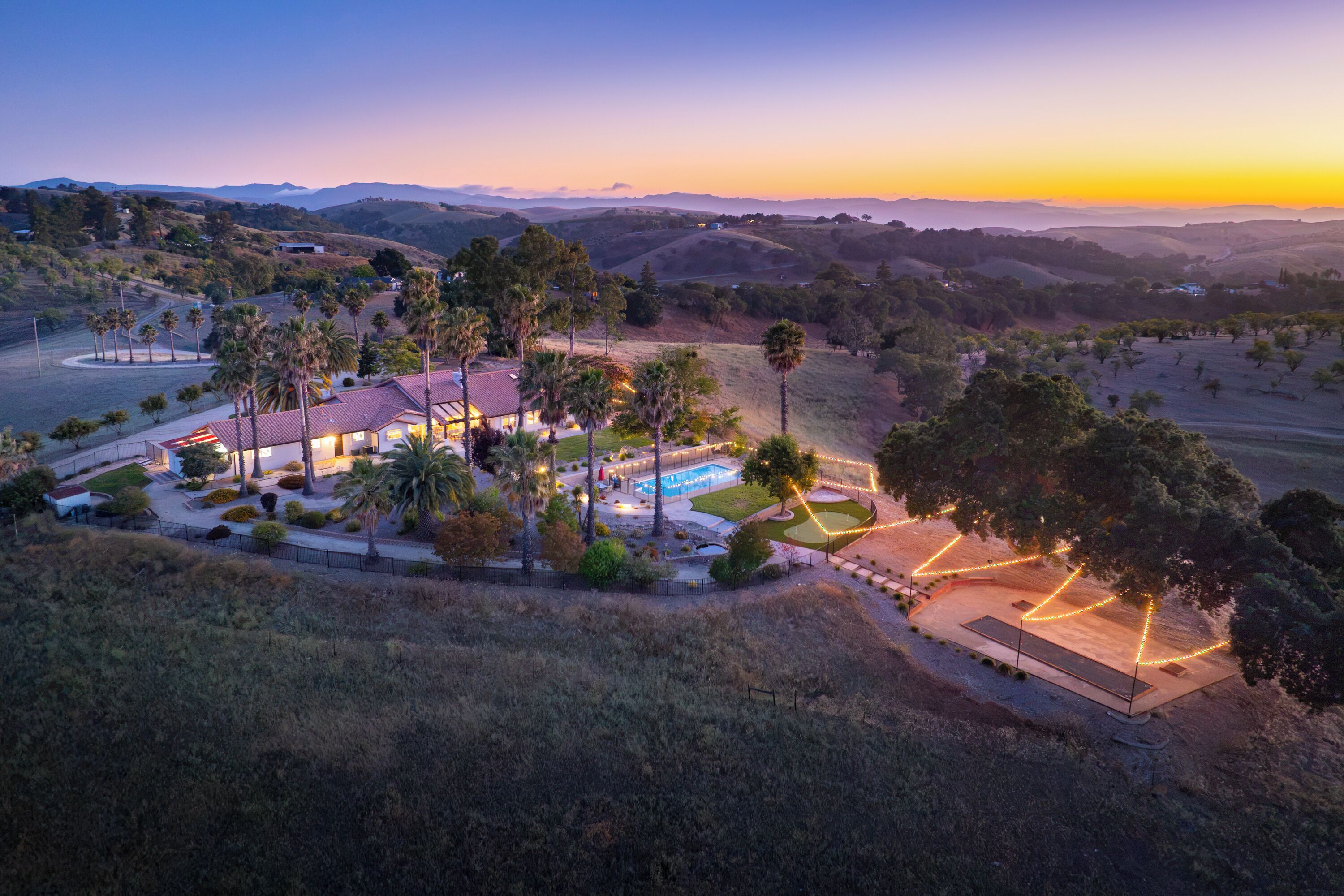 A large house with a swimming pool surrounded by palm trees and a hilly landscape.