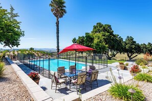A swimming pool with a red umbrella, surrounded by chairs and potted plants. - Hilltop Oasis (Templeton)
