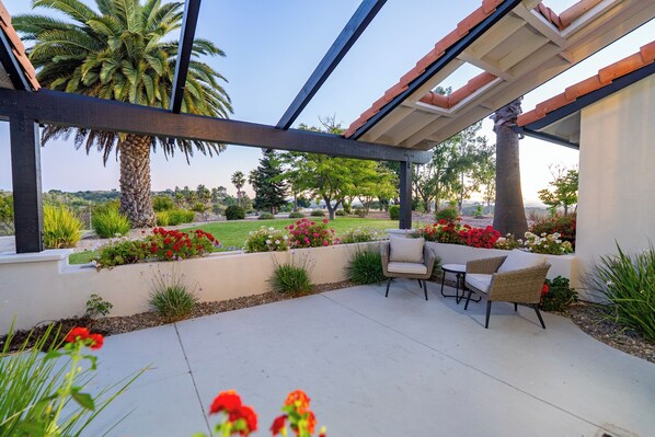Un patio exterior con pérgola, zona de estar y vistas a un jardín ajardinado.