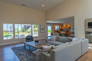 A spacious living room with a large sofa, a coffee table, and a view of the outdoor patio. - Hilltop Oasis (Templeton)