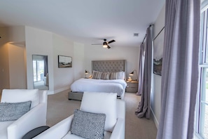 A hotel room with a bed, two chairs, a ceiling fan, a nightstand, and a window with curtains. - Hilltop Oasis (Templeton)