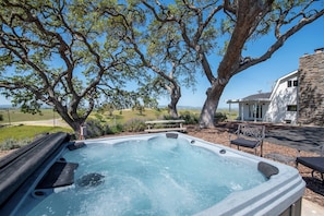 A hot tub with a stone exterior, surrounded by a patio area with outdoor furniture, a stone wall, and a large tree. - Hidden Acre - Bird House (Paso Robles)