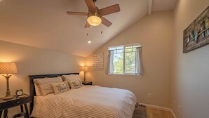 A bedroom with a bed, a ceiling fan, a nightstand with a lamp, a window, and a wall art piece. - Hidden Acre - Bird House (Paso Robles)