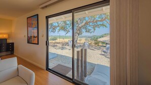 A modern living room with a large sliding glass door leading to an outdoor patio with a view of a tree and a gravel area. - Heartview Cottage (Templeton)