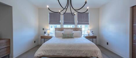 Un dormitorio espacioso con una cama grande, una araña de cristal, lámparas de noche y un banco de madera.