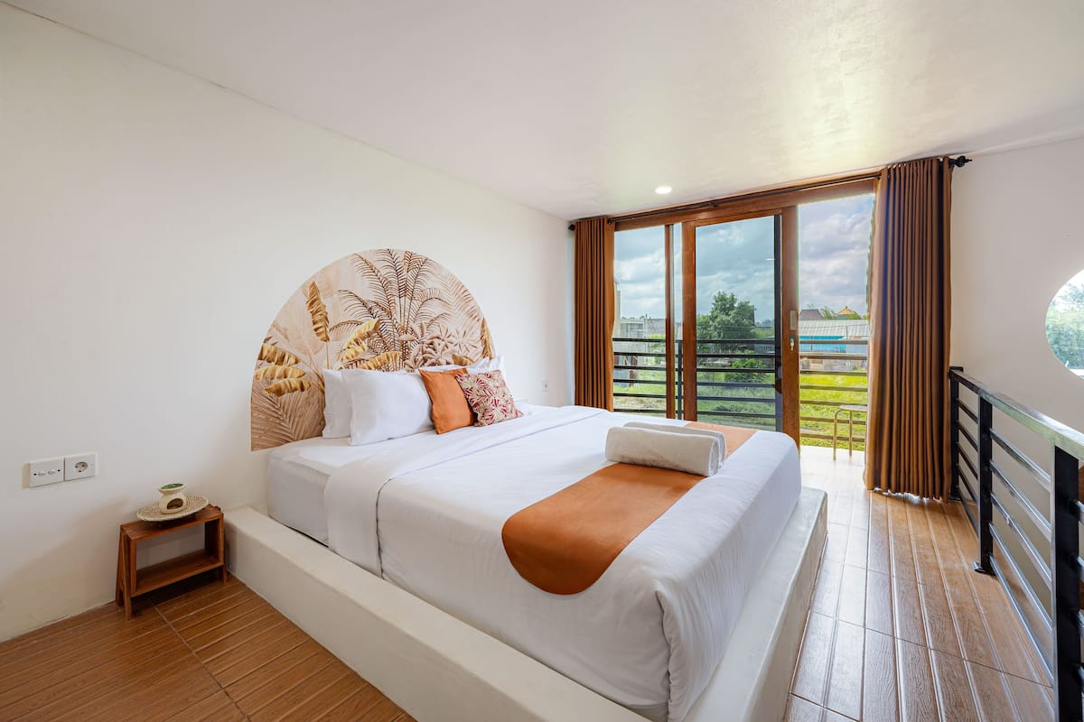 Une chambre à coucher avec un grand lit, une petite table de chevet, une fenêtre avec des rideaux et une vue sur l’extérieur.