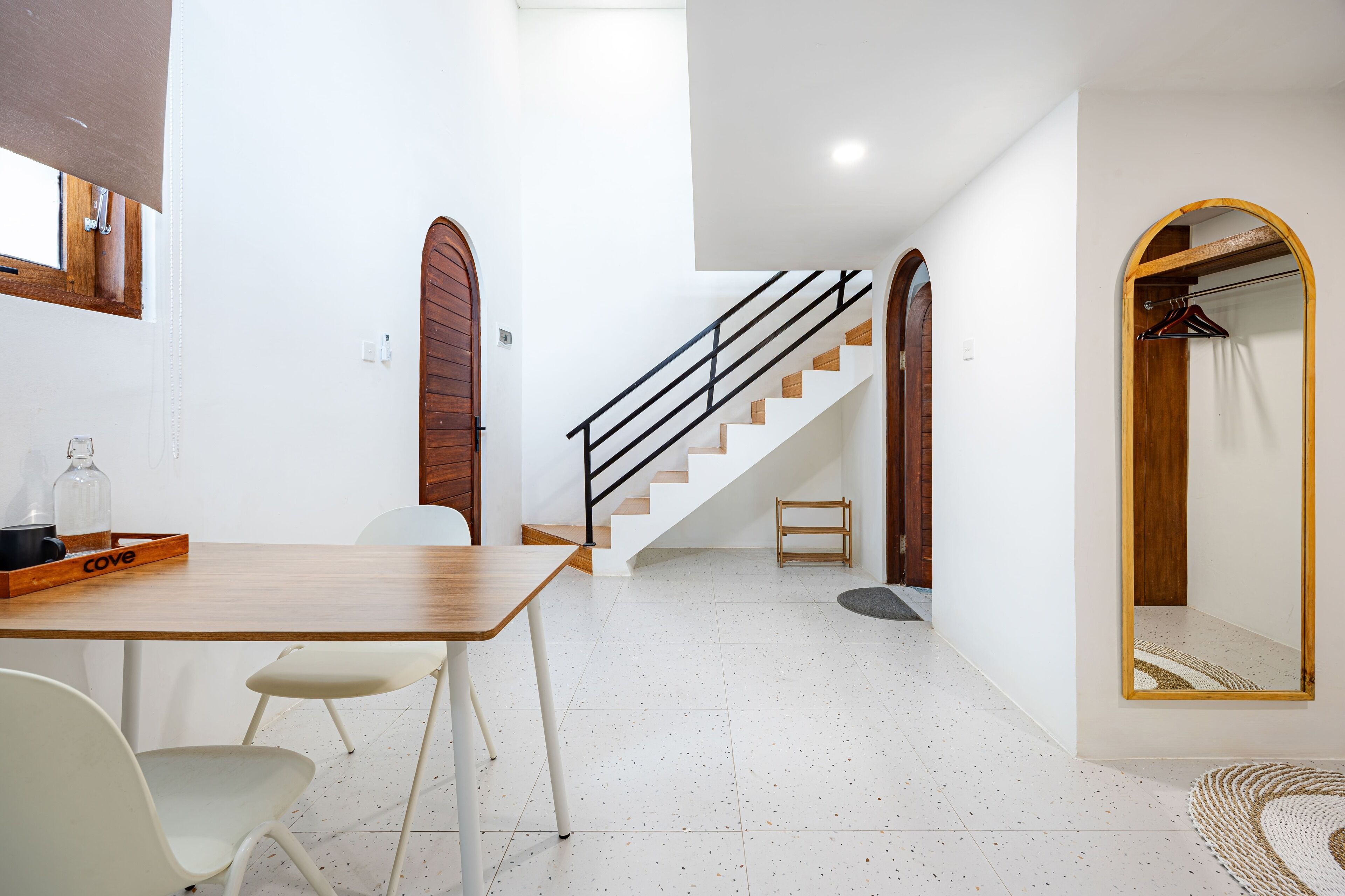 Un interior moderno con una mesa de comedor de madera, sillas blancas, una escalera y un espejo con marco de madera.