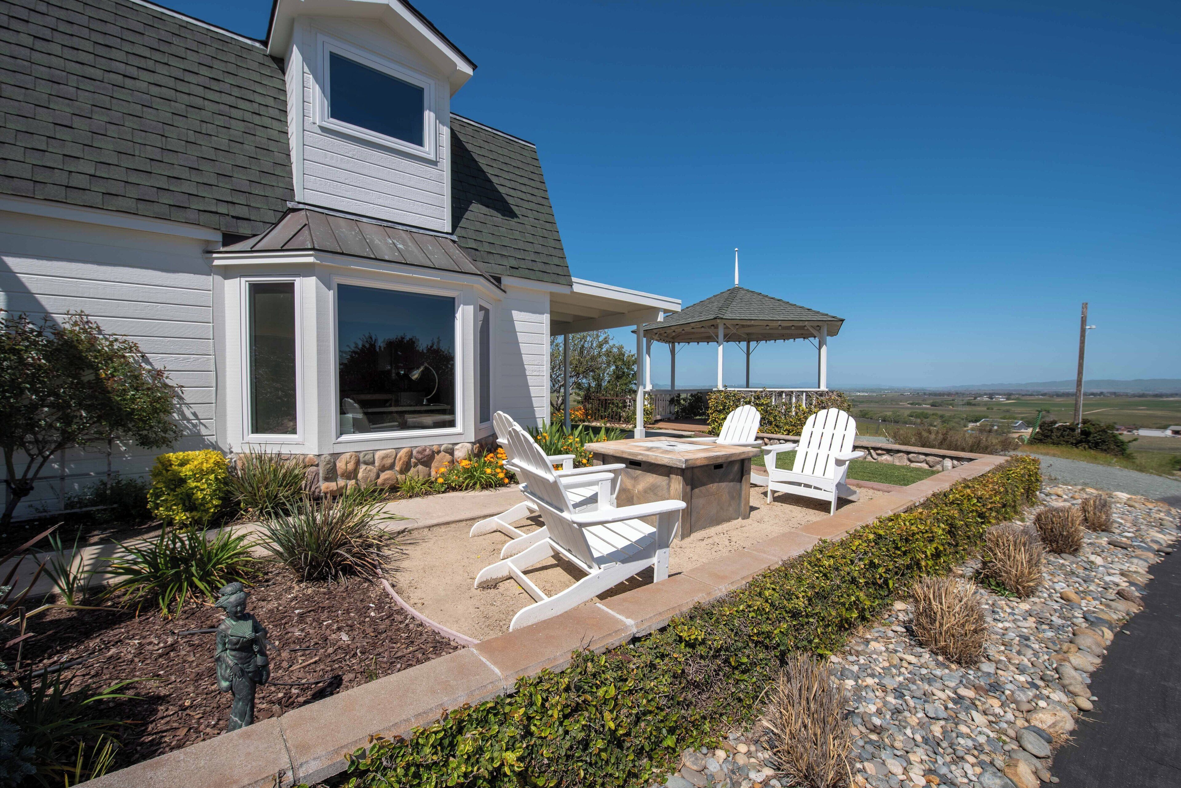 A house with a covered patio area featuring Adirondack chairs and a stone fire table.