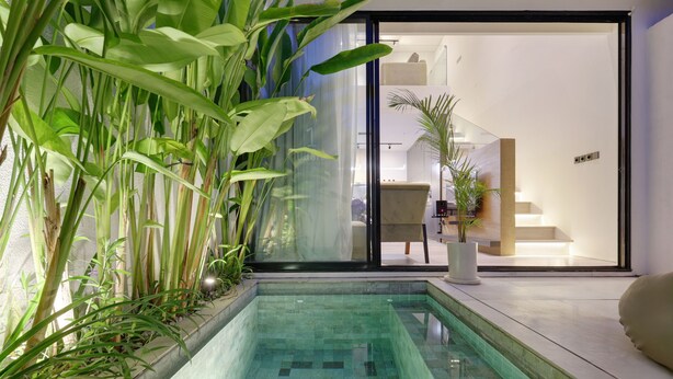 Une piscine intérieure moderne, dotée d’une eau cristalline et entourée de grandes plantes vertes.