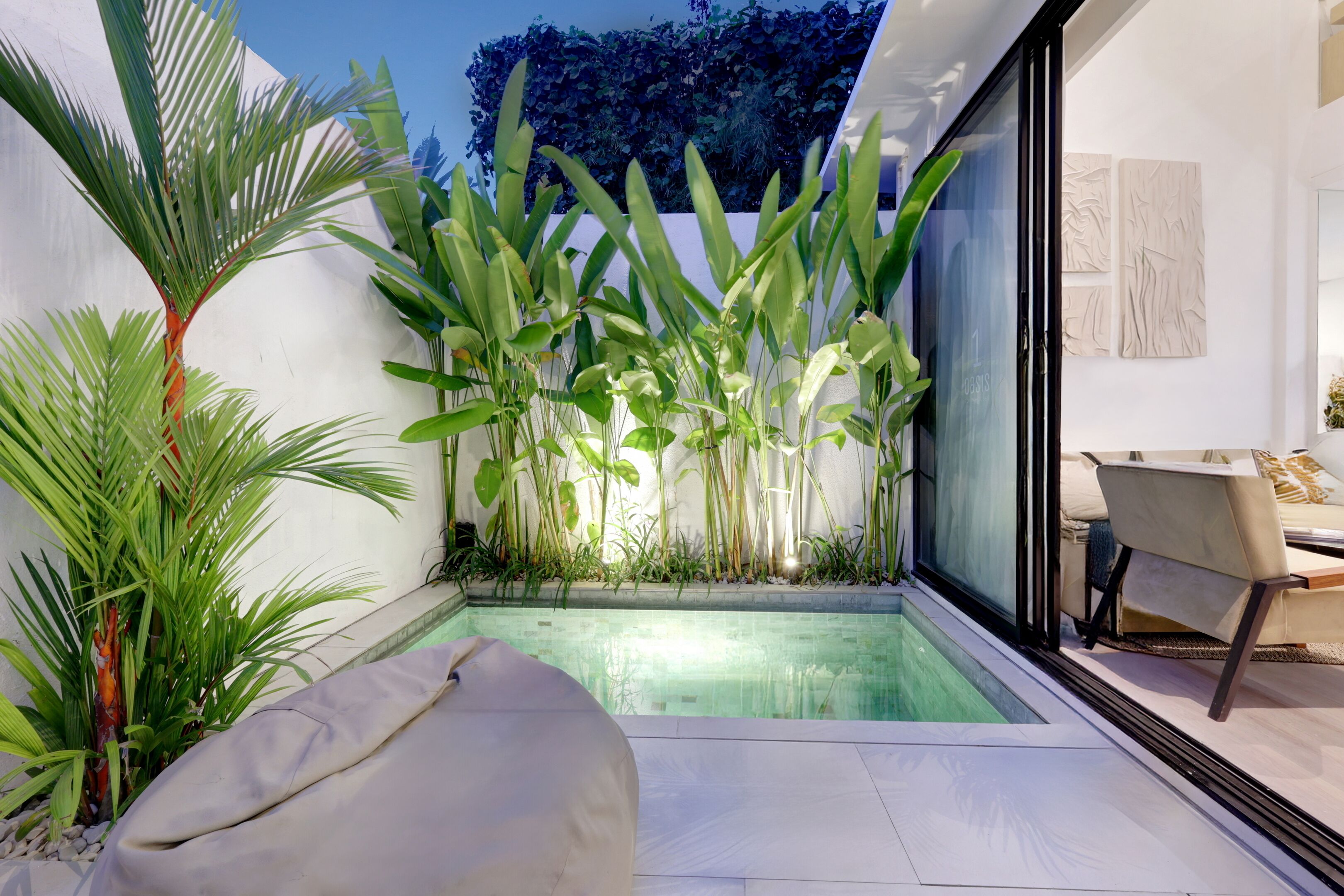 A modern outdoor pool area with a minimalist design, surrounded by lush greenery and a comfortable seating area.