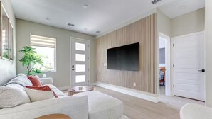 Ein modernes Wohnzimmer mit einem Ecksofa, einem Flachbildfernseher an einer Wand aus Holzpaneelen und einer Topfpflanze.