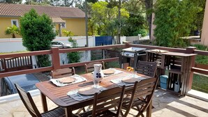 Un espace extérieur aménagé pour les repas, avec une table et des chaises en bois, un barbecue et une vue sur le quartier.