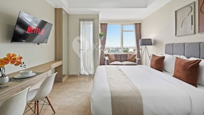 A hotel room with a bed, a desk, a TV, and a view of the city. - Brenna by Kozystay - Menteng (Jakarta)