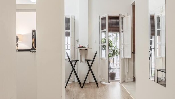 Um interior moderno com piso de madeira, paredes brancas e uma área de refeições com duas cadeiras pretas e uma mesa pequena.