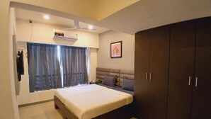 A bedroom with a bed, a wardrobe, a ceiling fan, an air conditioning unit, and a window with curtains.