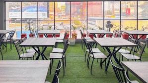 An indoor dining area with tables and chairs, large windows with a view of the city, and a motivational quote on the wall.