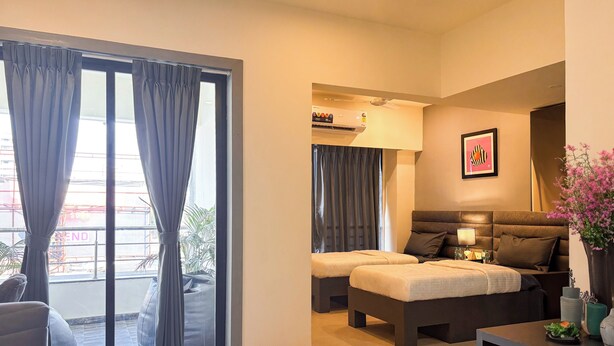 A modern hotel room with a sofa, two beds, a desk, and a large window with curtains.