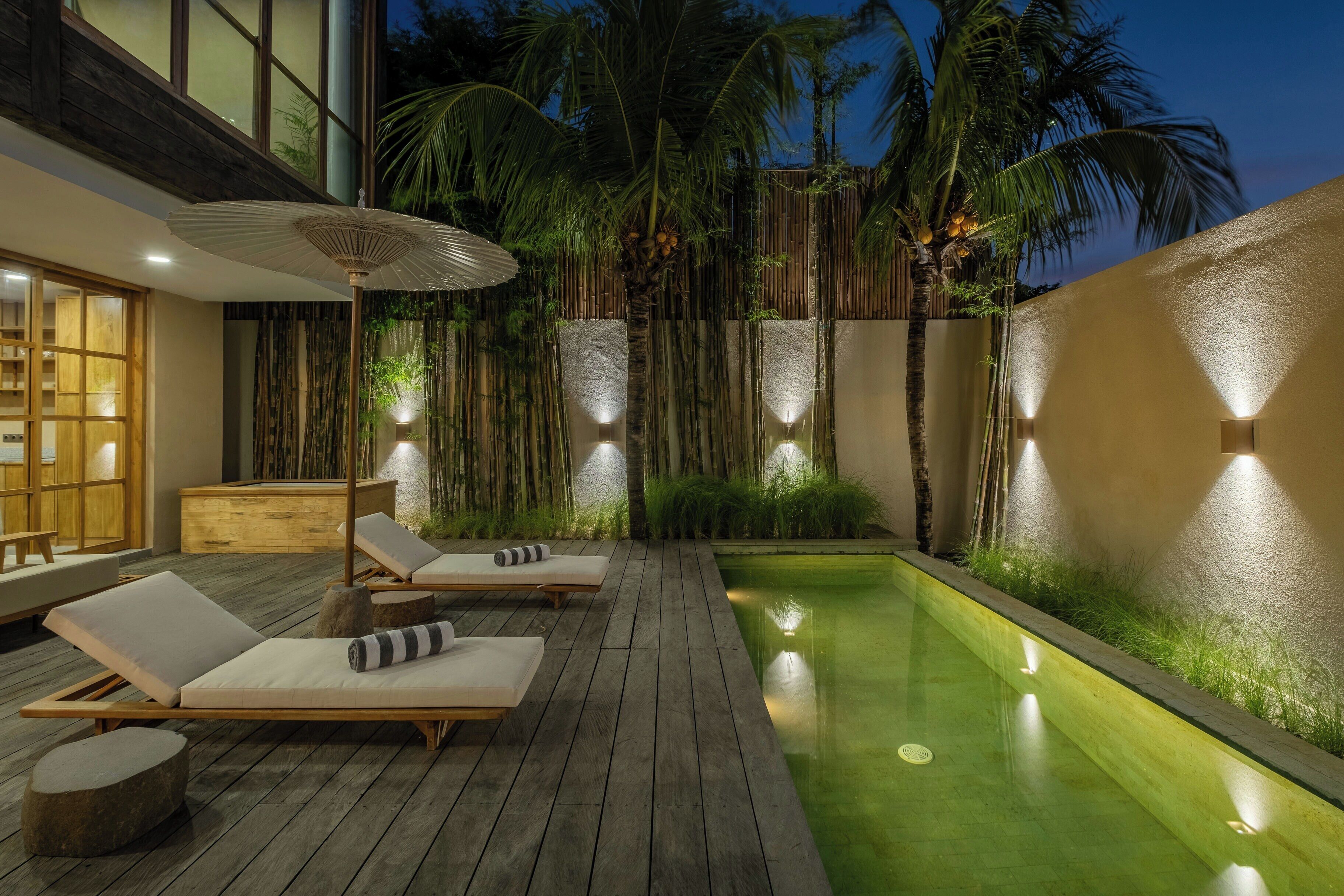 Une terrasse en bois avec des chaises longues et une petite piscine, entourée de murs en bambou et de palmiers.